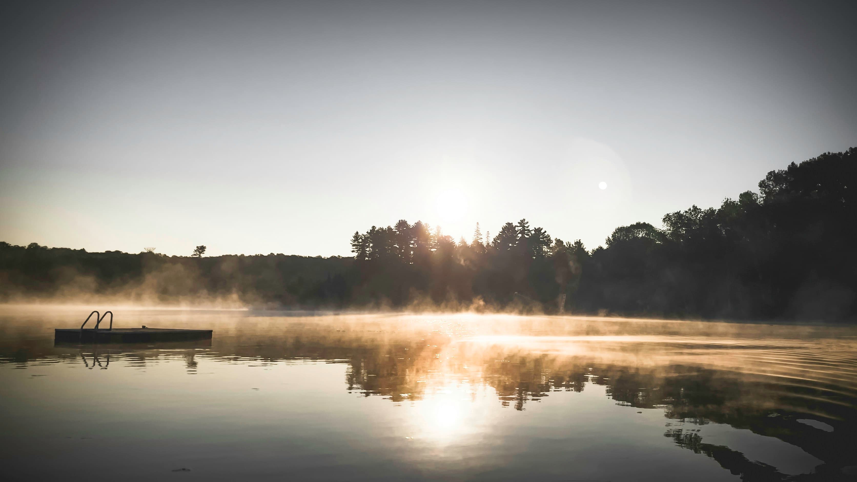Misty sunrise over a still lake with a small dock
