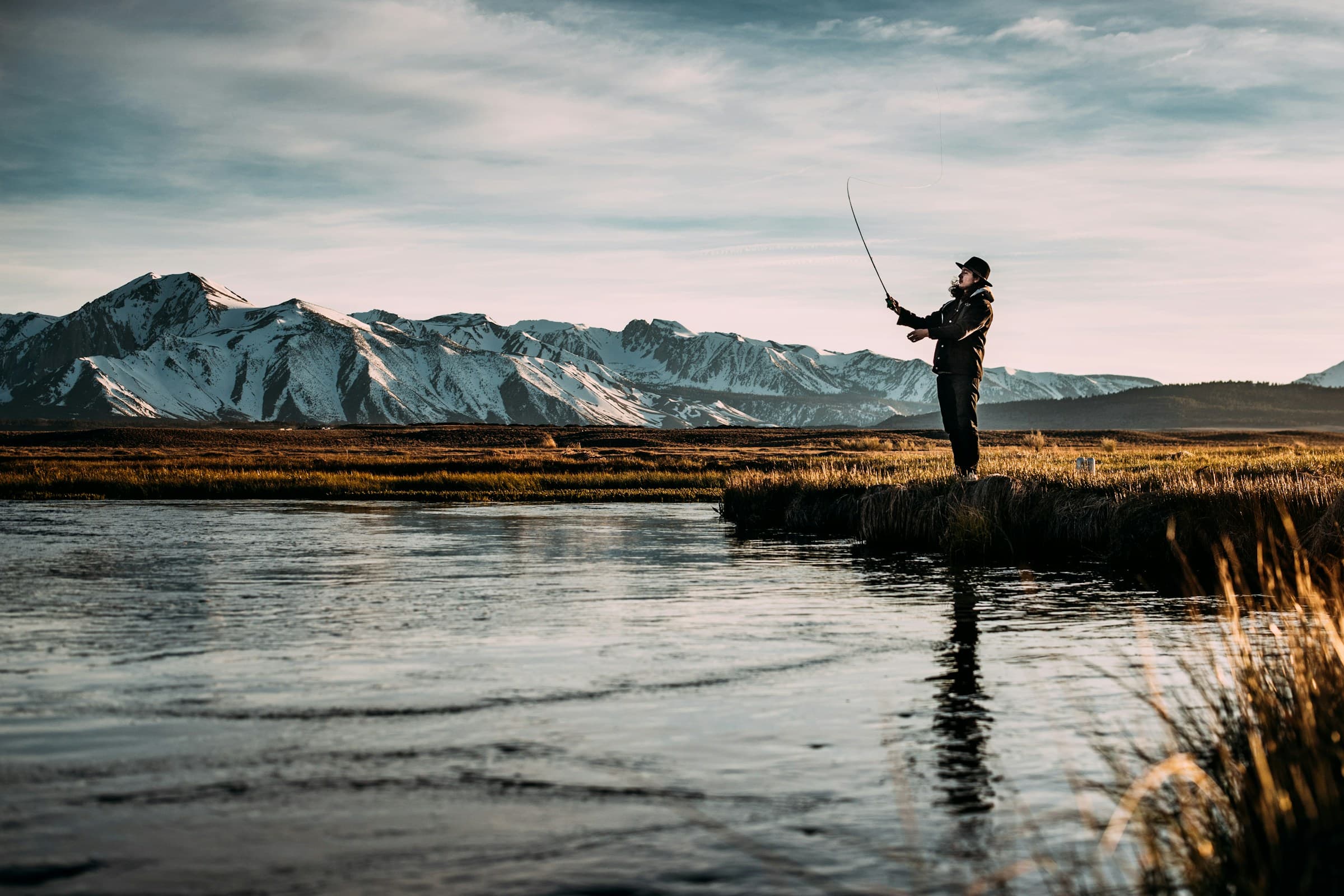 Fly angler wading a river at dusk with mountains behind